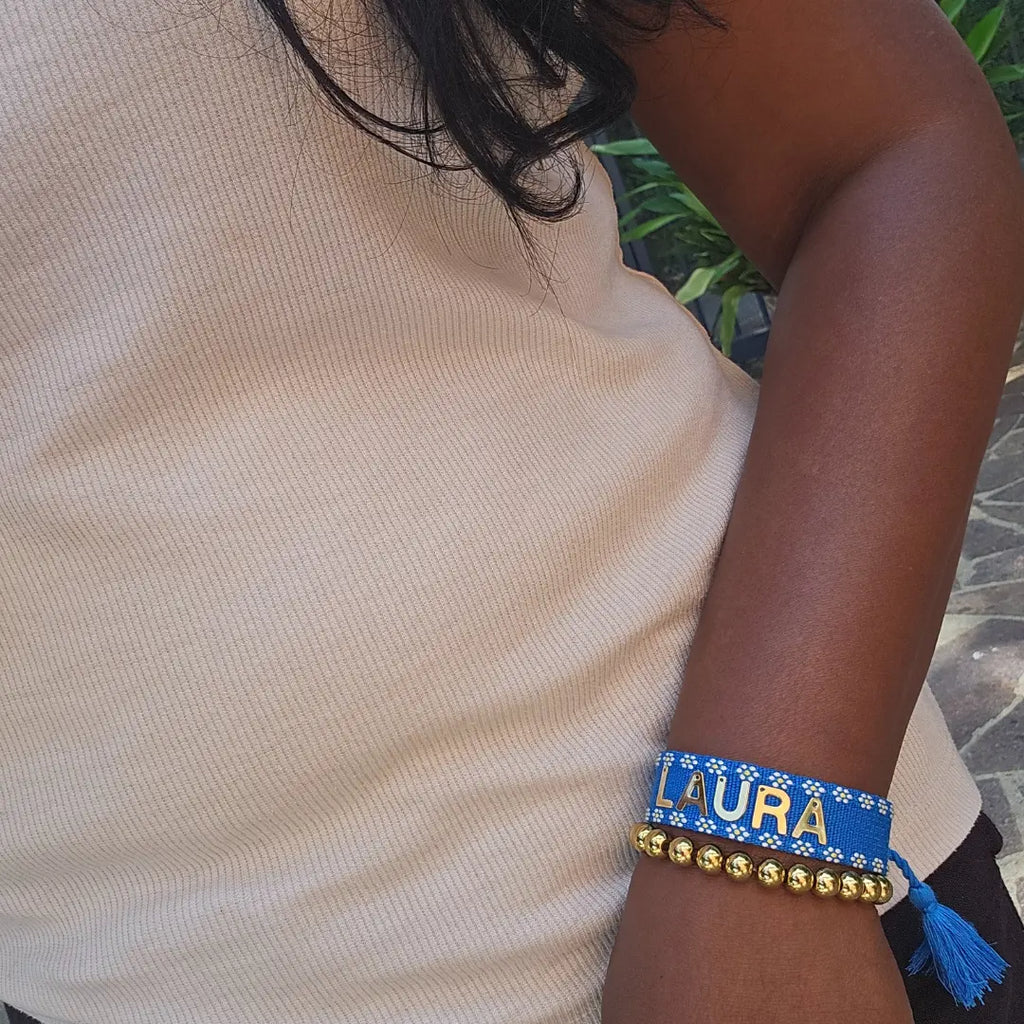 bracciale in filo blu con bordi con fiori bianchi, con nappa regolabile, personalizzato con nome in acciaio inox colore oro. Regalo personalizzato unisex per ogni occasione, anche per auto regalo per persone uniche