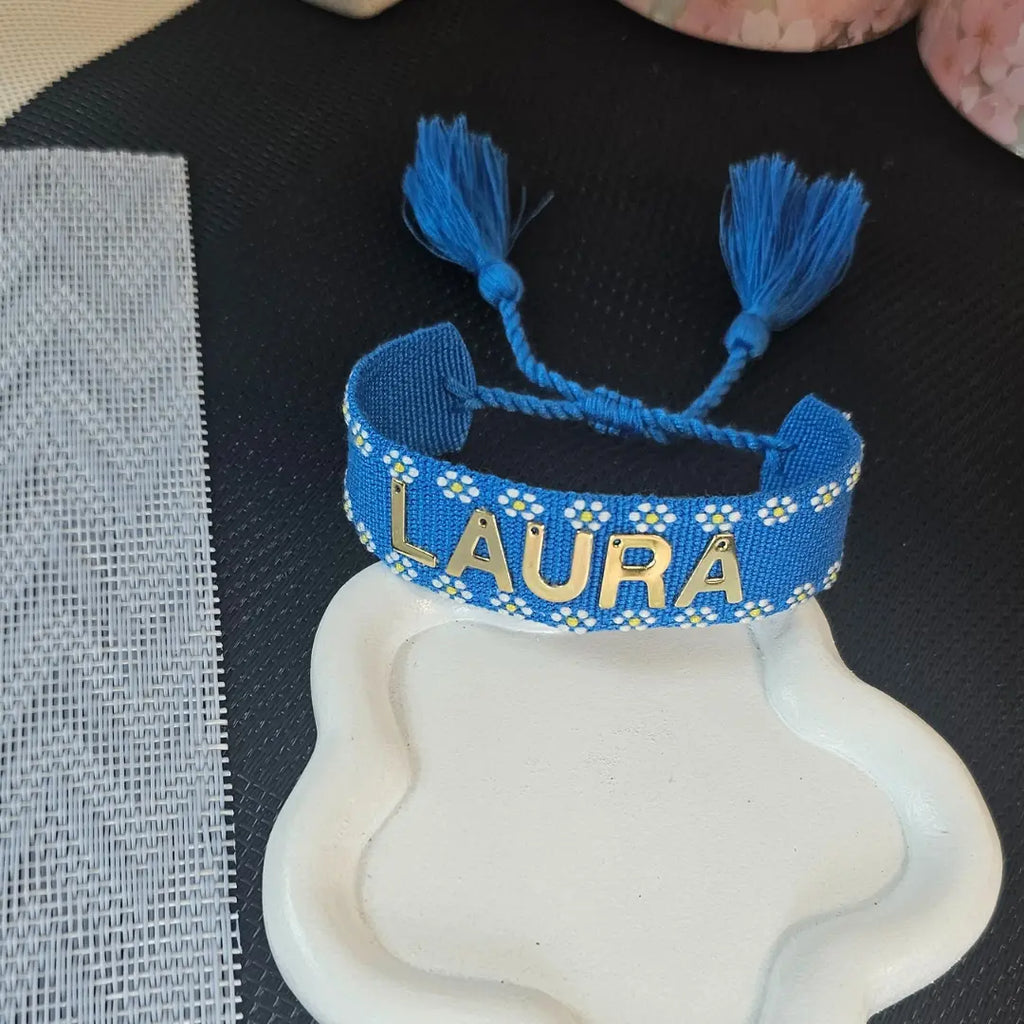 bracciale in filo blu con bordi con fiori bianchi, con nappa regolabile, personalizzato con nome in acciaio inox colore oro. Regalo personalizzato unisex per ogni occasione, anche per auto regalo, regalo originale