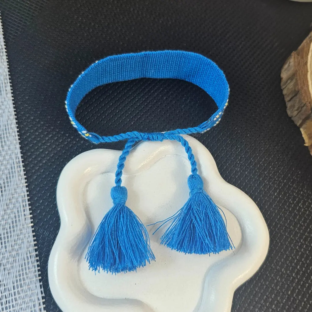 bracciale in filo blu con bordi con fiori bianchi, con nappa regolabile, personalizzato con nome in acciaio inox colore oro. Regalo personalizzato unisex per ogni occasione, anche per auto regalo. Per qualsiasi polso.